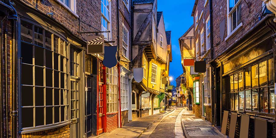 View down narrow, cobbled street with timber-framed buildings jutting out over and into the street at dusk. 