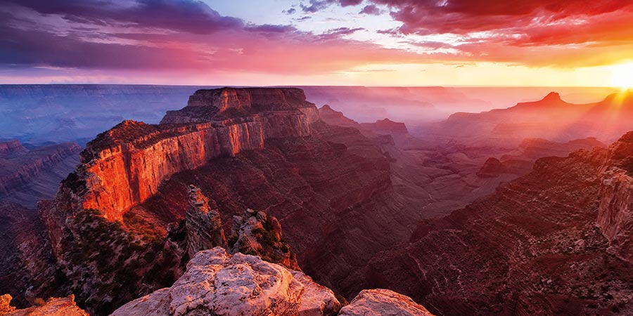 The grand canyon is bathed in orange, red and purple light at a dramatic sunset. 